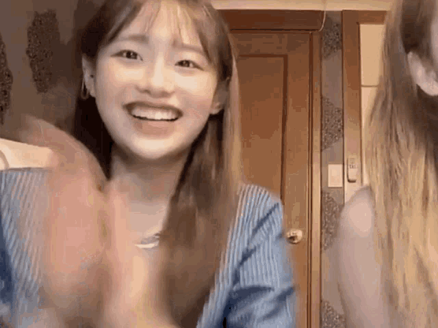a woman in a blue striped shirt is smiling and clapping her hands .