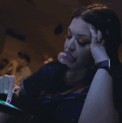 a woman blowing a bubble while looking at a phone