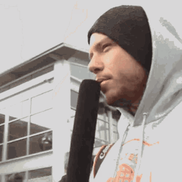 a man wearing a hoodie and a beanie holds a microphone in his mouth