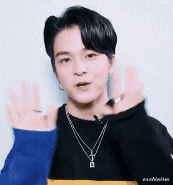a young man wearing a blue and yellow striped sweater and a cross necklace is waving his hands .