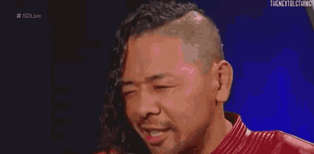 a man with long hair is wearing a red leather jacket and laughing with his eyes closed .