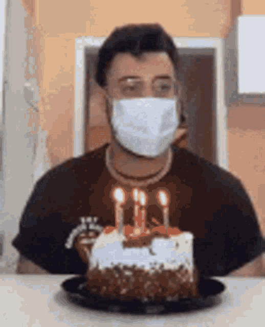 a man wearing a mask is blowing out three candles on a birthday cake .