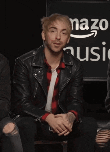 a man in a black leather jacket sits in front of an amazon music logo