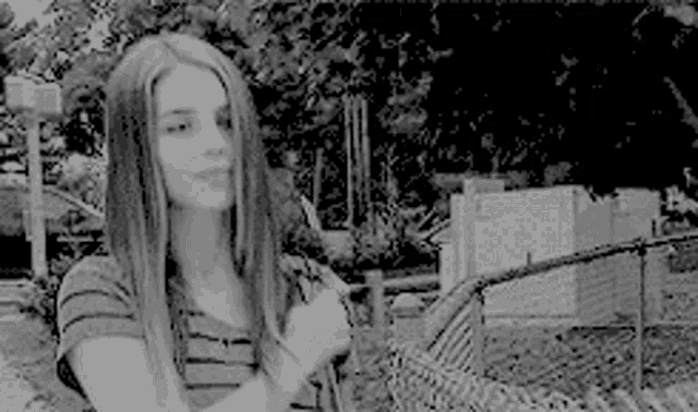 a woman with long hair is standing in front of a fence .