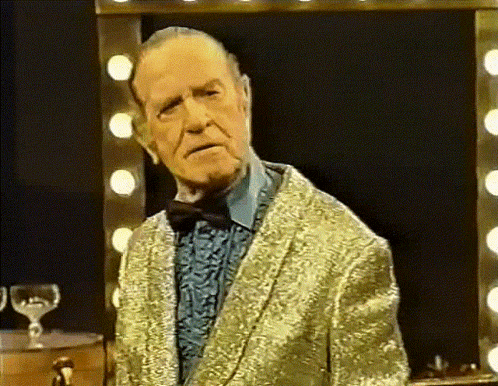 an older man in a gold suit and bow tie stands in front of a mirror
