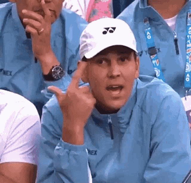 a man wearing a white hat and a yonex jacket is giving the middle finger .
