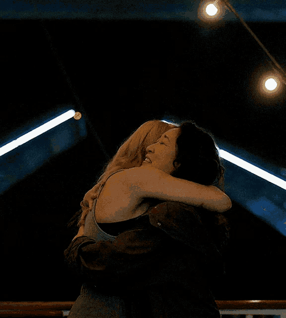 two women hugging each other in the dark with lights behind them