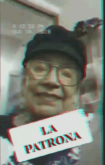 a man wearing glasses and a black hat holds a sign that says la patrona