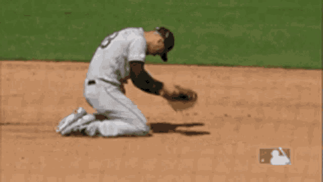 a baseball player is kneeling down on the field while throwing the ball .