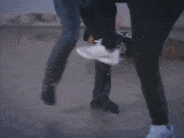 a man is laying on the ground in the rain while another man kicks him .