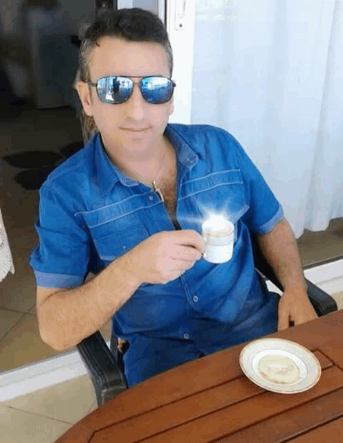 a man wearing sunglasses sits at a table with a cup of coffee