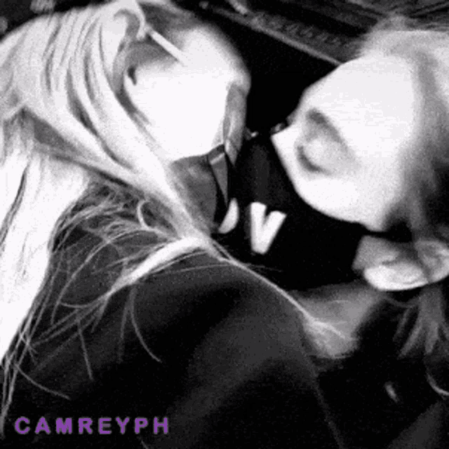 two women are kissing each other in a black and white photo with the name camreyph written on the bottom .