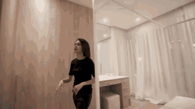 a woman in a black dress is standing in a bedroom next to a dressing table .