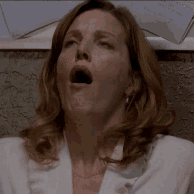 a woman in a white coat is yawning in front of a wall with papers on it