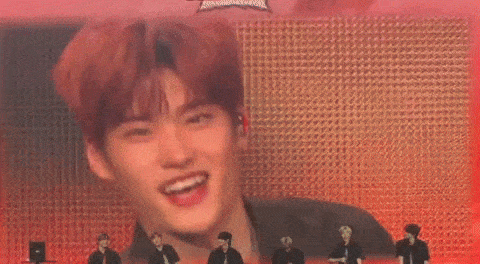 a man with red hair is standing in front of a large screen with a group of men standing behind him .