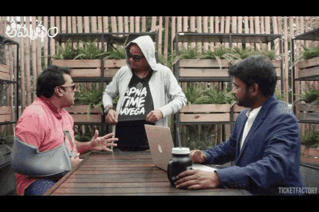 a man wearing a shirt that says apna time navega talks to another man