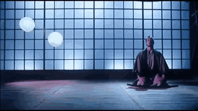 a man in a kimono sits on the floor in front of a window with squares on it