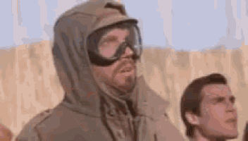 a man wearing a hooded jacket and goggles is standing in the sand .