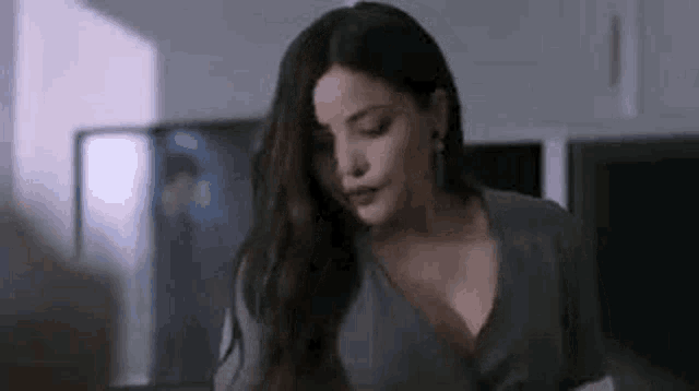 a woman with long hair and a plunging neckline is standing in a kitchen .