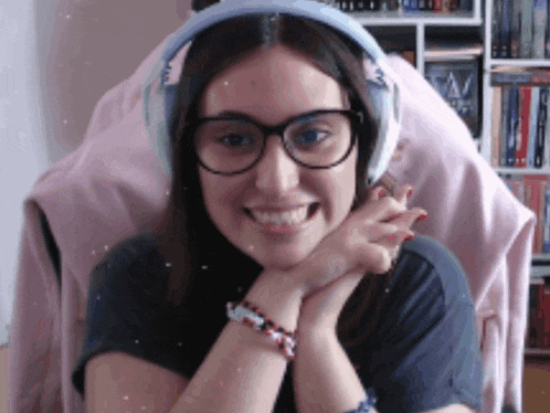 a woman wearing glasses and headphones smiles with her hands on her chin