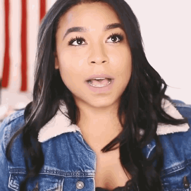 a woman wearing a denim jacket with a fur collar looks surprised
