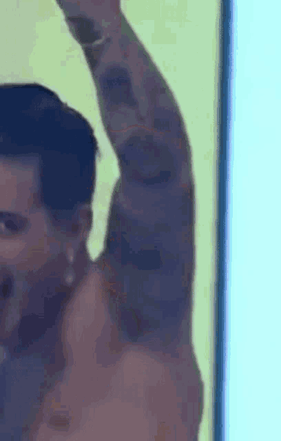 a shirtless man with a tattoo on his arm is standing in front of a wall with his arm in the air .