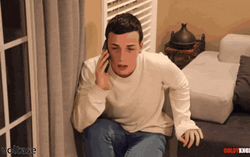 a man sitting on a couch talking on a cell phone with voltage written on the bottom right