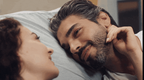 a man with a beard and a woman laying on a bed looking at each other