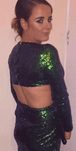 a woman in a green sequined dress with a cut out back is standing in front of a white wall .