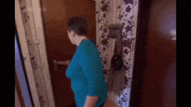 a woman in a blue shirt is standing in a hallway holding a door handle .