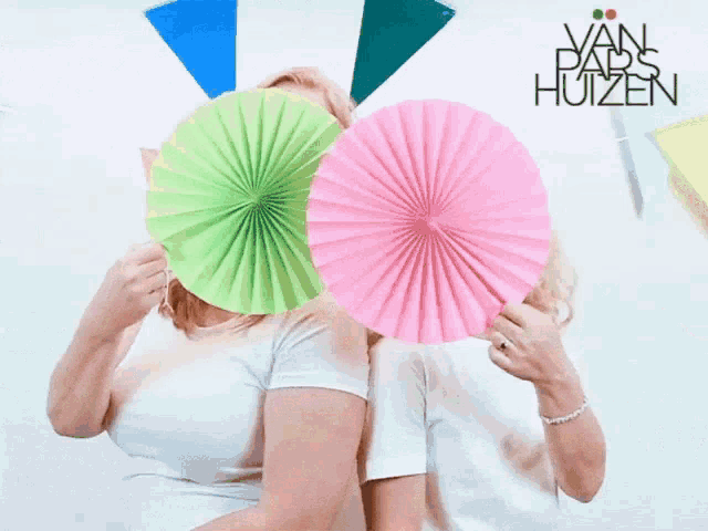 two women are holding paper fans in front of their faces in front of a sign that says van paps huisen