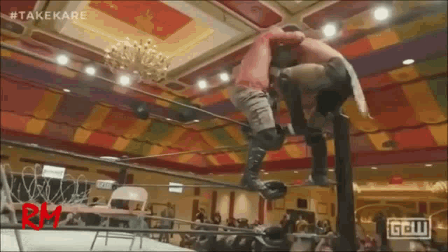 two men are wrestling in a ring in a room with a crowd watching .