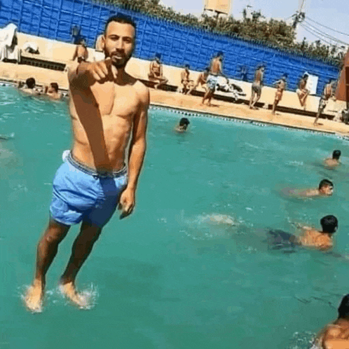 a shirtless man is jumping into a swimming pool while people are swimming in it .