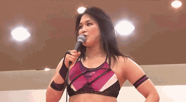 a woman in a pink and purple top is holding a microphone to her mouth