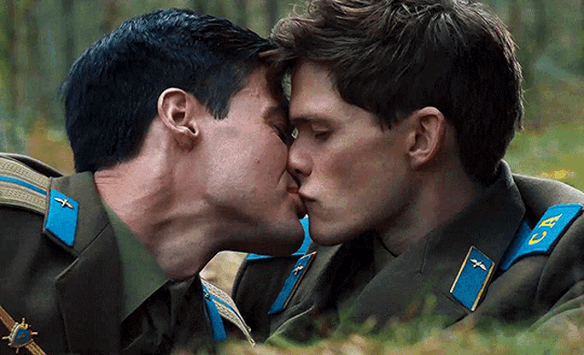 two men in military uniforms are kissing and one has the letter u on his collar
