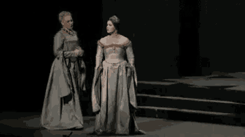 two women are standing next to each other on a stage in medieval costumes .