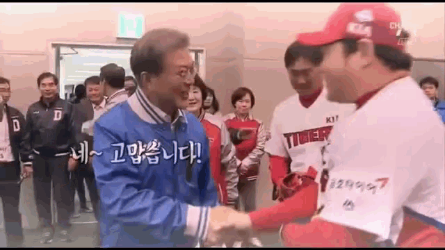 a man in a blue jacket shakes hands with a baseball player wearing a red hat .