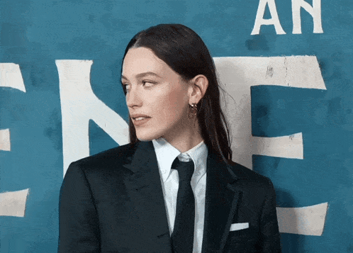 a woman in a suit and tie is standing in front of a sign that says an