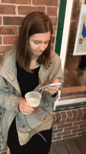 a woman drinking a cup of beer while looking at her phone