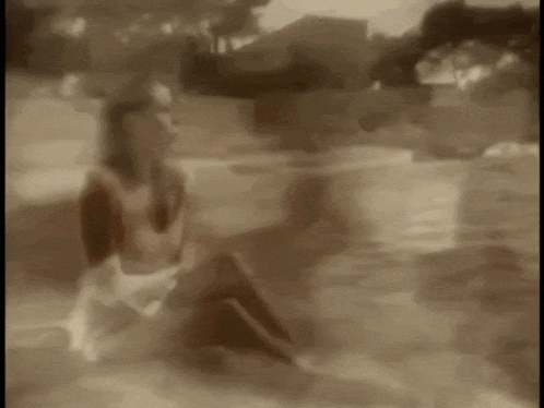a woman in a white dress sits on the edge of a swimming pool