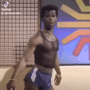 a man in a black tank top and blue shorts is dancing in front of a wall .