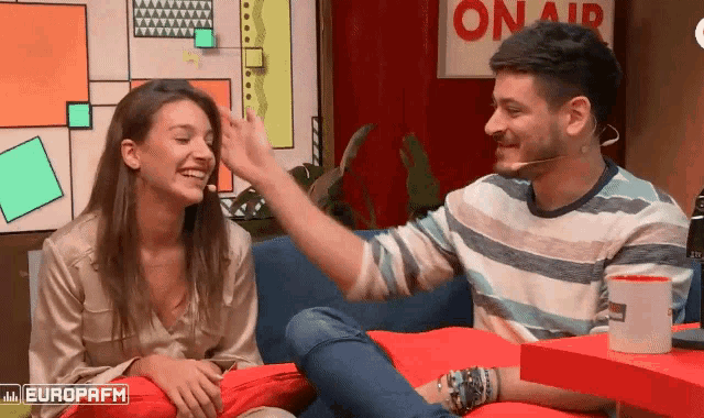 a man is touching a woman 's forehead in front of a sign that says " on air "