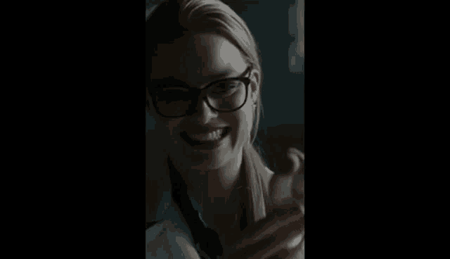a woman wearing glasses and a lab coat is smiling while holding a cell phone .