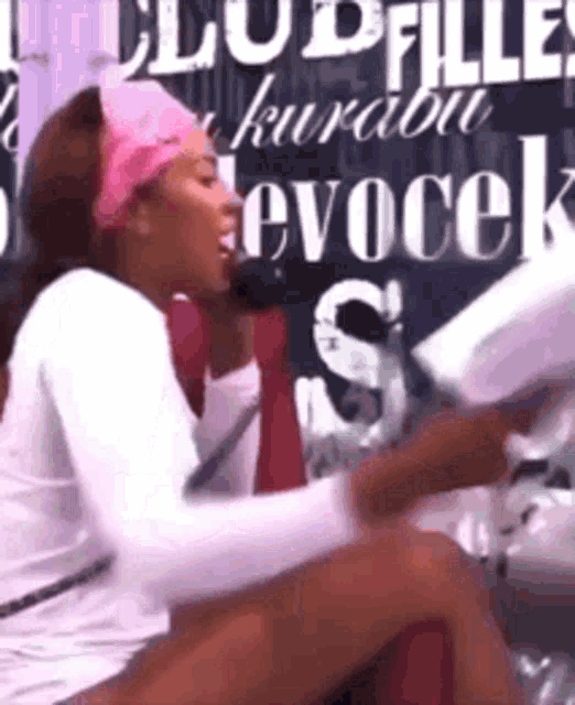 a woman wearing a pink headband and a white shirt is sitting in front of a sign that says evocek .