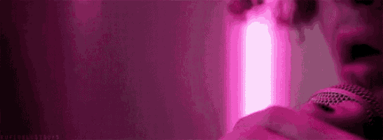 a close up of a person singing into a microphone with a pink light behind them .