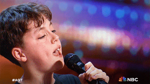 a young boy singing into a microphone with nbc written on the bottom