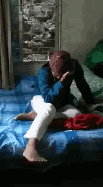 a man is sitting on a bed covering his face with his hands .