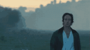a man in a white shirt is standing in a field at sunset .