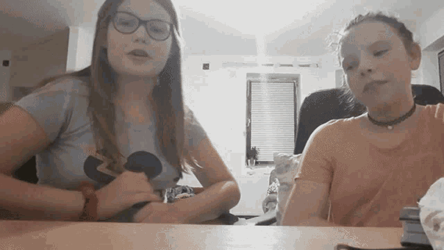 two girls are sitting at a table with one wearing a mickey mouse t-shirt