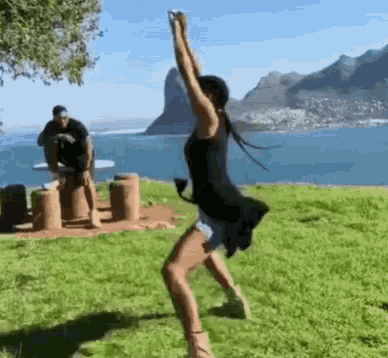 a woman is dancing in a park with a man taking a picture of her in the background .